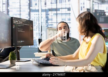 Man with paraplegia drinking coffee, checking colleague doing code review to fix bugs in software. Woman debugging and optimizing code using AI, supervised by manager in wheelchair enjoying beverage Stock Photo