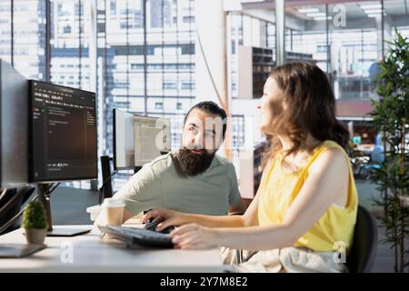 Programmer doing software debugging, asking for help from team leader in wheelchair. Employee fixing coding mistakes, being assisted by manager with disability in inclusive workplace Stock Photo