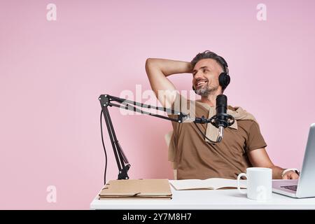 Relaxed man in headphones using microphone while recording podcast against pink background Stock Photo