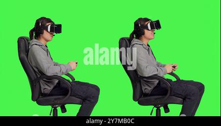 Player enjoying game with virtual reality headset and controller while engaging in digital gaming event with other people. Asian guy resting on chair against greenscreen scene, vr gadget. Stock Photo