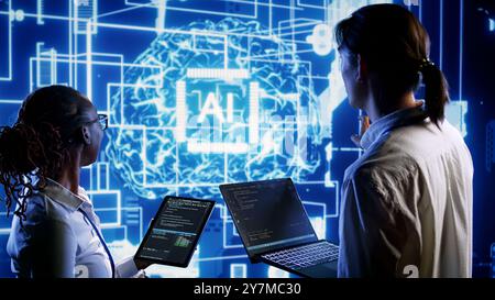 Teamworking colleagues updating AI systems, writing intricate binary code scripts on tablet and laptop. Qualified engineers using programming to upgrade artificial intelligence simulation model Stock Photo