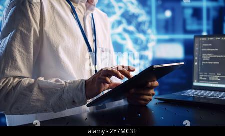Computer scientist in data center, solving tasks on tablet while running programming scripts on laptop terminal. Certified engineer manipulating lines of code for AI applications development Stock Photo