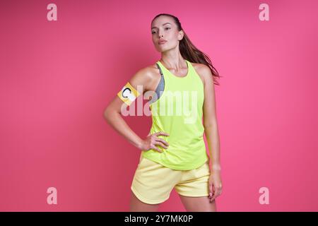 Confident woman in sports clothing wearing captain band while standing against pink background Stock Photo