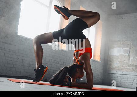 Beautiful young African woman doing handstand splits in gym Stock Photo