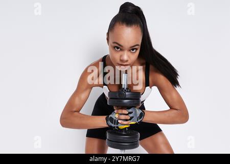 Concentrated young African woman holding dumbbell while standing against white background Stock Photo