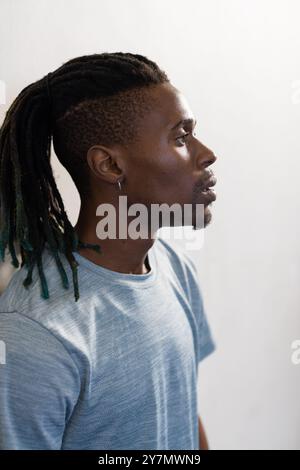 Looking thoughtful, man with dreadlocks wearing blue shirt in profile view Stock Photo