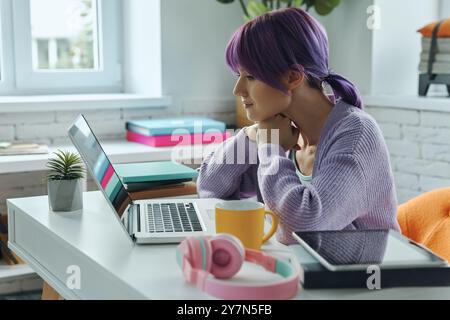 Concentrated young woman with purple hair working on laptop while sitting at her working place Stock Photo