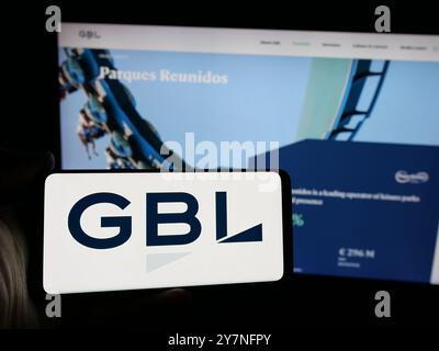 Person holding smartphone with logo of company Groupe Bruxelles Lambert S.A. (GBL) on screen in front of website. Focus on phone display. Stock Photo