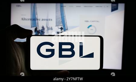 Person holding cellphone with logo of company Groupe Bruxelles Lambert SA (GBL) on screen in front of business webpage. Focus on phone display. Stock Photo