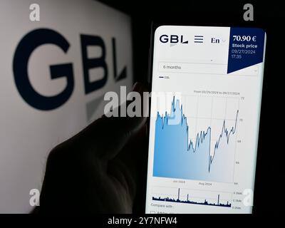 Person holding cellphone with website of company Groupe Bruxelles Lambert S.A. (GBL) on screen in front of logo. Focus on center of phone display. Stock Photo