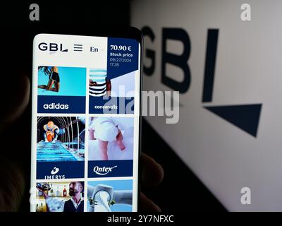 Person holding smartphone with webpage of company Groupe Bruxelles Lambert S.A. (GBL) on screen with logo. Focus on center of phone display. Stock Photo