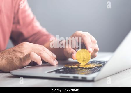 Man holds a golden Bitcoin while using a laptop, representing Bitcoin as a form of digital currency for online transactions, highlighting the concept Stock Photo
