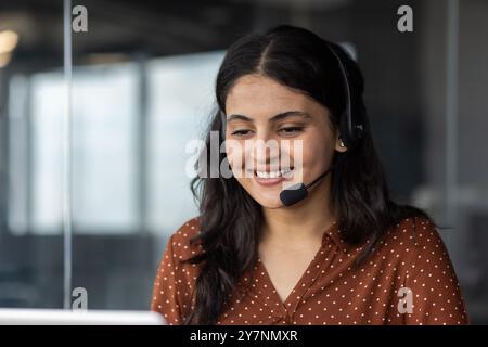 Young woman in office wearing headset engaged in customer service call smiling while communicating with clients providing assistance and support through phone showing, professionalism and dedication. Stock Photo