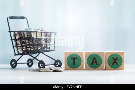 TAX is written on a wooden block and coins in a shopping cart on a wooden table against a bright white background. Commercial tax and Financial planni Stock Photo