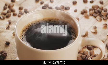 White cup of hot steaming coffee on a wooden table and roasted coffee beans near it. Stock Photo