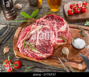 Raw beef steaks with herbs and spices ready for cooking are on wooden board. Stock Photo