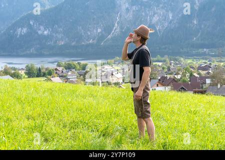 An elderly Tyrolean man, 50-55 years old, wearing traditional clothes, sings and shouts against the backdrop of a village surrounded by mountains, Stock Photo