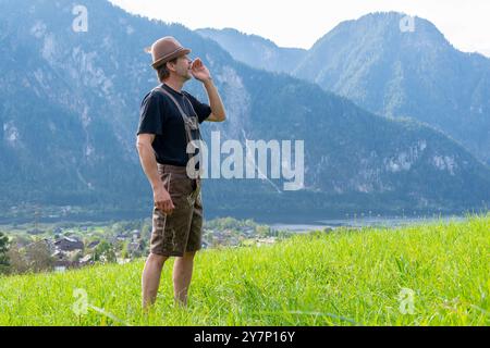 An elderly Tyrolean man, 50-55 years old, wearing traditional clothes, sings and shouts against the backdrop of a village surrounded by mountains, Stock Photo