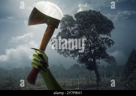 Witch hand with long black nail holding axe in with full moon in the background. The axe is bloody and hand is green. Evil, satan, zombie or monster h Stock Photo