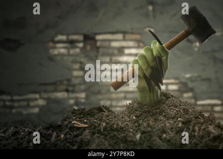 Witch hand with long black nail coming out from grave ground holding a hammer with brick wall background. The hand appearing to be a evil, satan, zomb Stock Photo