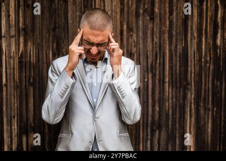 Portrait of young businessman who is having headache. Wooden background. Stock Photo