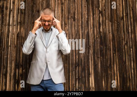 Portrait of young businessman who is having headache. Wooden background. Stock Photo