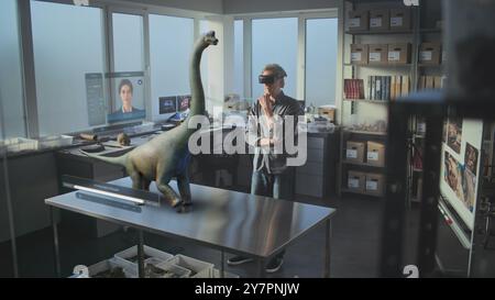 Advanced archaeological lab: 3D graphics of virtual display with AI assistant, animation of ancient dinosaur species. Archaeologist in VR headset conducts scientific research using augmented reality. Stock Photo