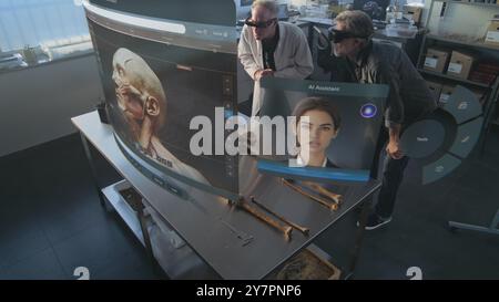 Modern archaeological lab: Two archaeologists in VR headsets study fossil skeleton using augmented reality technology. VFX graphics of virtual display with AI assistant and 3D modeling app interface. Stock Photo