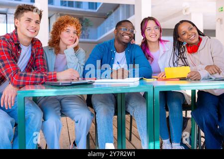 Multiethnic group of students sitting with a laptop gleefully looking at camera Stock Photo