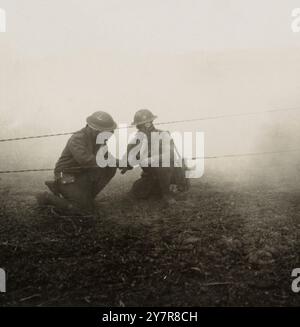 Repairing field telephone lines during a gas attack at the front. 1914-1918 Photograph shows two soldiers wearing gas masks, kneeling to repair telephone lines in a cloud of poisonous gas at the front during World War I. Stock Photo