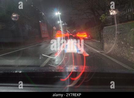 street scene at night through the windshield featuring a car with their break lights on. Stock Photo