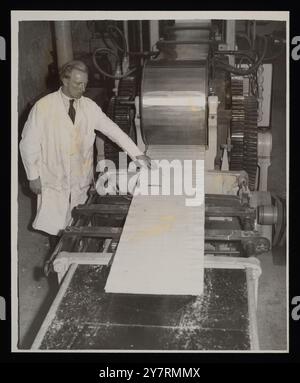 Britain can roll out ‘man-made lumber’ in any length. - London: ‘Man-made lumber’ - compressed sawdust bonded with resin - rolls from the machine at the Camden Town (North West London) research centre of the British Artificial Resin Company, which - with the aid of high frequency radio waves, infra-red heat, and electromagnetic vibrations -  has solved the problem of making this board in any length. Leading plastics scientists and teams of research workers have been working ten years on the problem of increasing the versatility of the board making plant. Previously, the board could be pressed Stock Photo