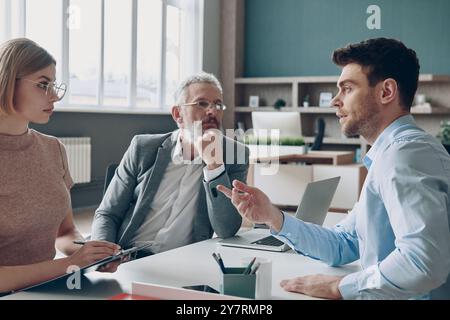 Handsome young man having interview with HR managers while sitting at the office desk Stock Photo