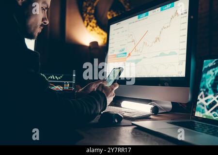 Close-up of confident young male stock trader using smart phone and computers while working late in office Stock Photo