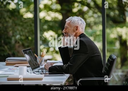 Confident mature businessman talking on mobile phone while sitting sat his working place in office Stock Photo