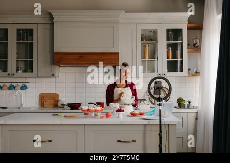 Beautiful young woman preparing cream for homemade cake and recording video for food blog Stock Photo