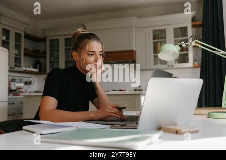 Bored young woman sitting at the desk and looking at laptop while studying at home Stock Photo