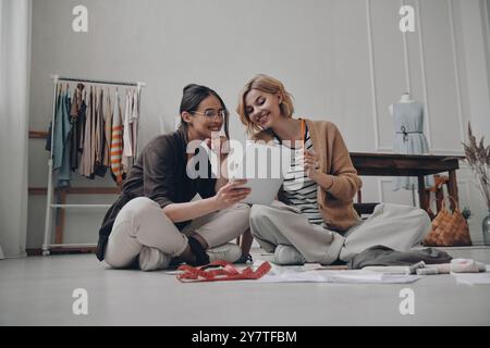 Two happy female fashion designers using digital tablet while working in workshop Stock Photo