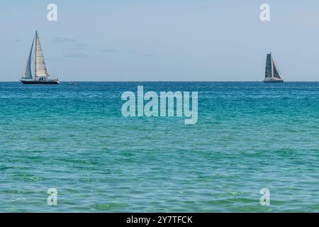 Two sailboats on the horizon sailing in opposite directions on the blue sea Stock Photo