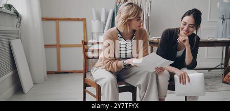 Two female fashion designers discussing new project while working in workshop Stock Photo