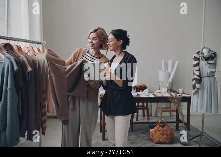 Two beautiful female fashion designers discussing clothes while working in workshop Stock Photo
