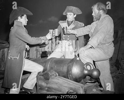 SALUTE TO (FILM) ADVENTURE Across a massive cannon on the deck of the ' Lydia ', Gregory Peck, as  ' Captain Hornblower, ' splices the main brace' with two tough henchman to mark the first day of filming of the new Warner pictures ' Captain Horatio Hornblower ' at Denham Studios, Bucks. On left is Robert Beatty, who plays Lieutenant Governor's, first officer of the '  Lydia  ', and on right James Robertson Justice, as Quist, ex-convict seamen and leader of the press-gang. Justice has another serious battle on hand - he is contesting North Angus and millions in the forthcoming general election. Stock Photo