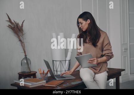 Confident young woman using technologies while sitting on the desk in creative office Stock Photo