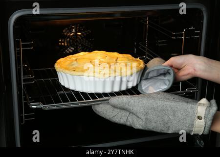 Woman putting homemade apple pie into oven in kitchen, closeup Stock Photo