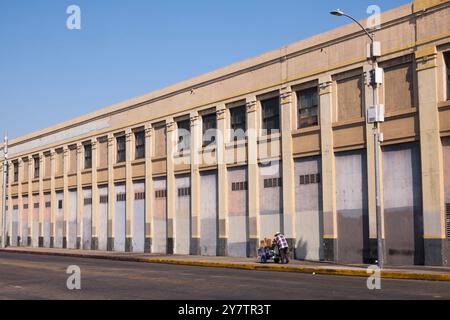 An old man pushes a cart in front of an old industrial building, Downtown Los Angeles, California, United States of America Stock Photo