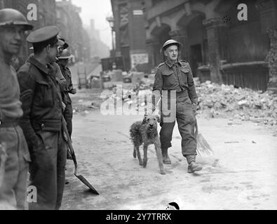 PIONEERS RELEASE DOG FROM AIR RAID DEBRIS AND GIVE IT A MEAL   Men of the Auxiliary Military Pioneer Corps engaged in clearing air raid debris in the London area discovered a dog which apparently had been buried for about three days.  The Pioneers gave the dog a meal and it appeared little the worse for its experience.  Photo shows:  A Pioneer leading away the dog after its release.  29 October 1940 Stock Photo