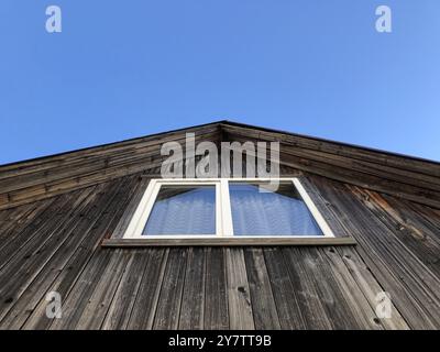 white window on the gable of a rustic wooden house, blue sky, low angle view Stock Photo