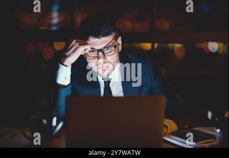 Serious Office Worker At Laptop Thinking Working Overnight At Workplace Stock Photo