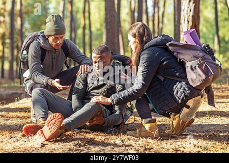 Friends helping african injured guy while hiking by forest Stock Photo