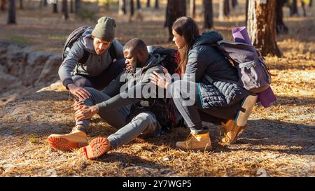 Friends helping black guy with injured leg, hiking at forest Stock Photo